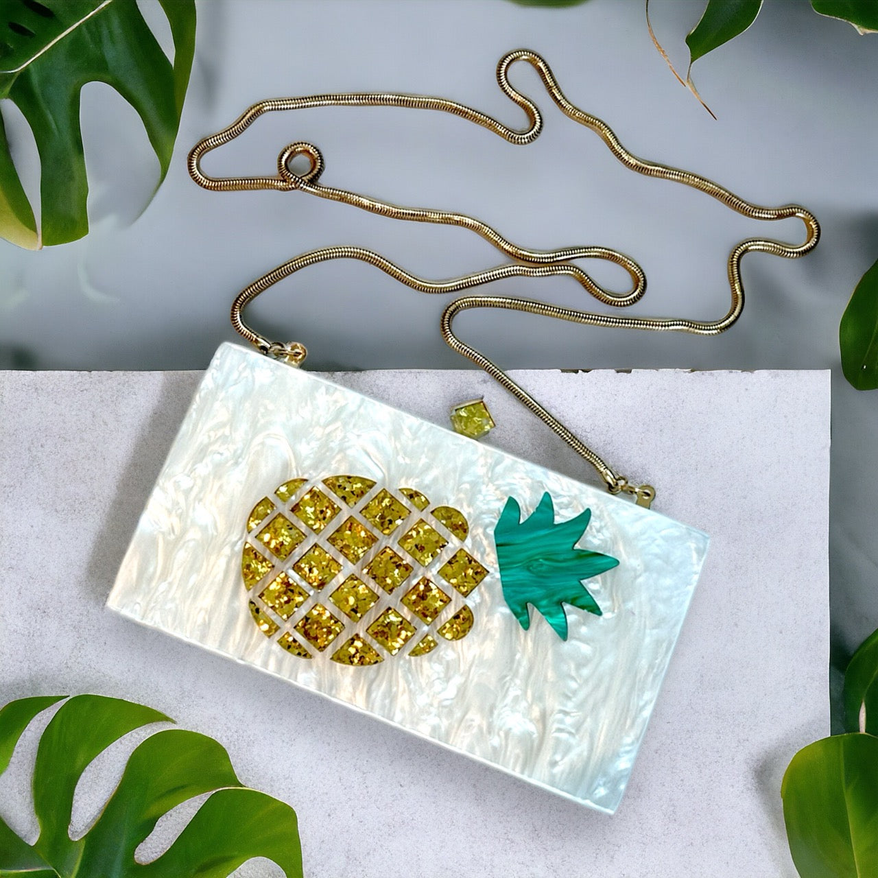 White clutch featuring beachy pineapple design with long gold chain hanging off it.