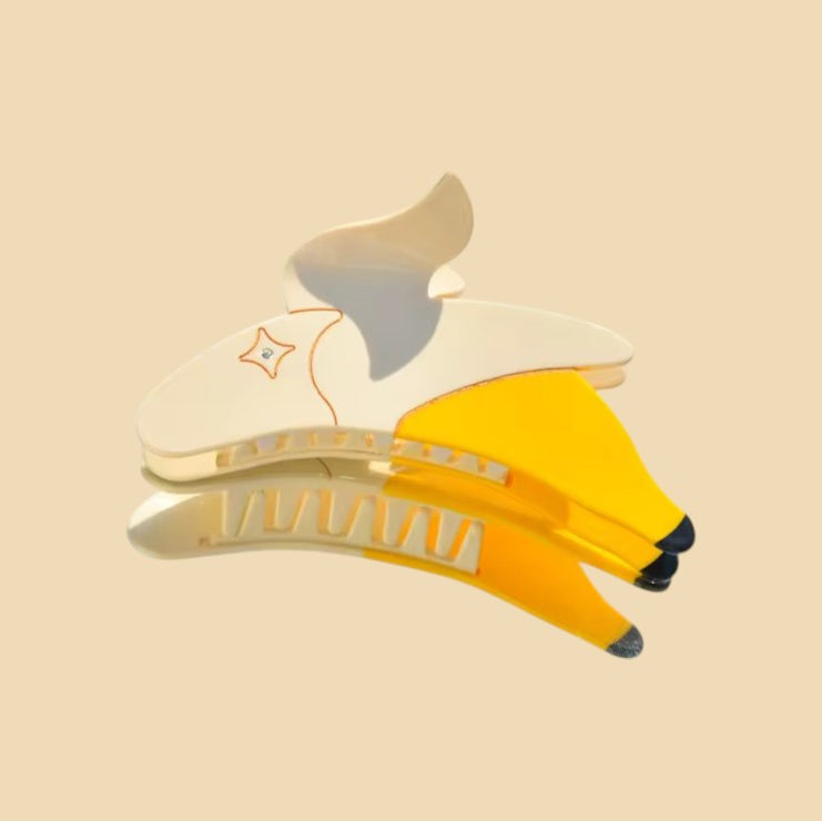 Yellow and white banana hair clip positioned on a light background.