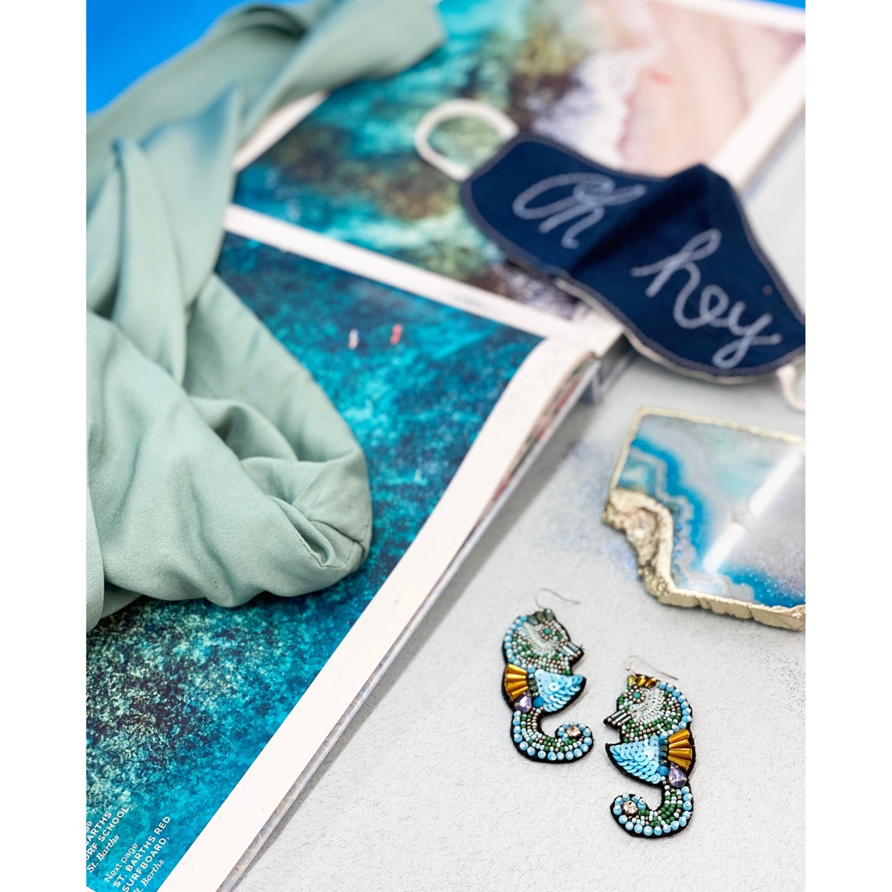 Handcrafted blue seahorse earrings with intricate beading and "Hi/Bye" design on the back.