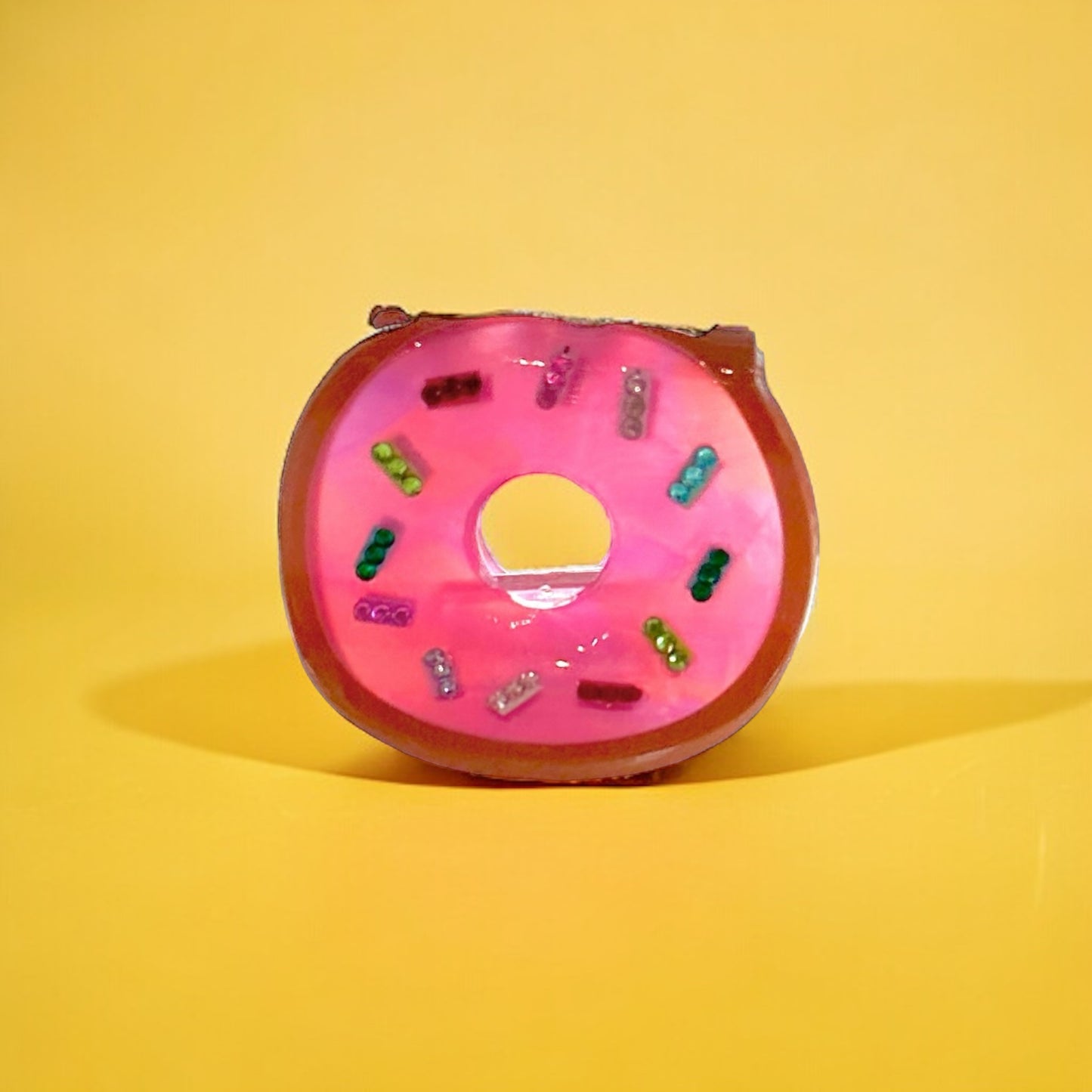 Donut-shaped hair clip with pink icing and a sprinkling of iridescent glitter.