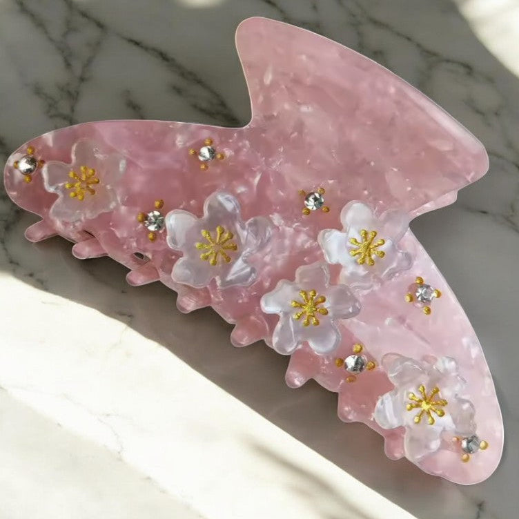 Pink floral butterfly hair clip on marble surface.