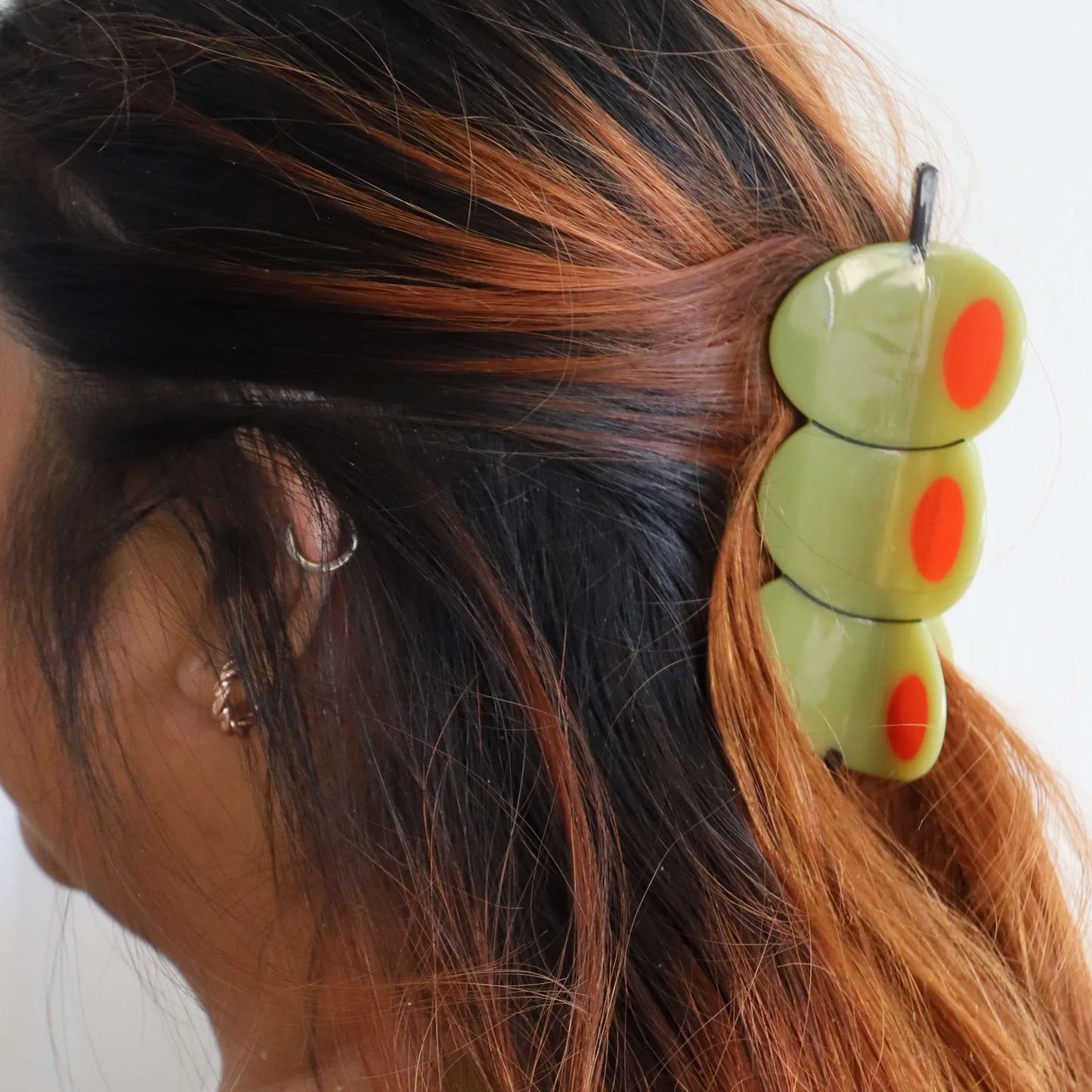 The olive skewer hair clip securing half-up brunette hair with caramel highlights, showcasing the full length and detail of the novelty accessory.