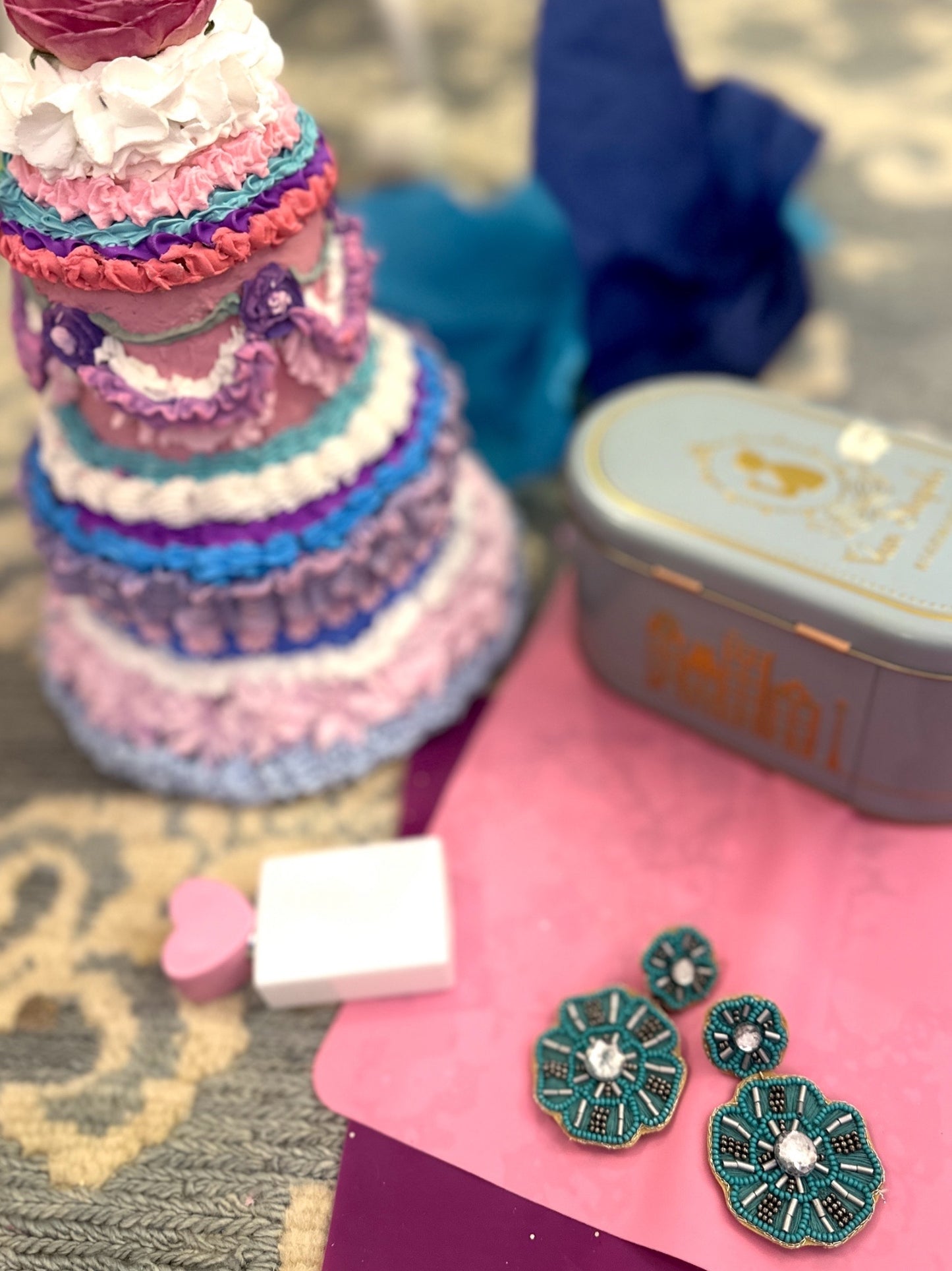 Aqua floral statement earrings displayed on a pink surface with a pastel frosted faux cake and teal vintage tin.