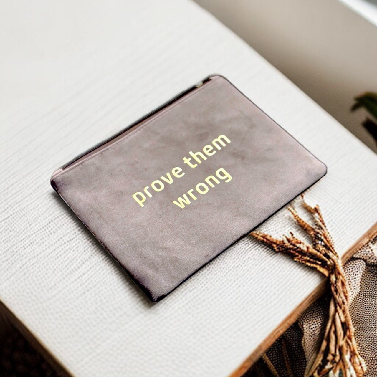 A statement accessory for women, featuring the motivational message "Prove Them Wrong" on a sleek and practical suede pouch.