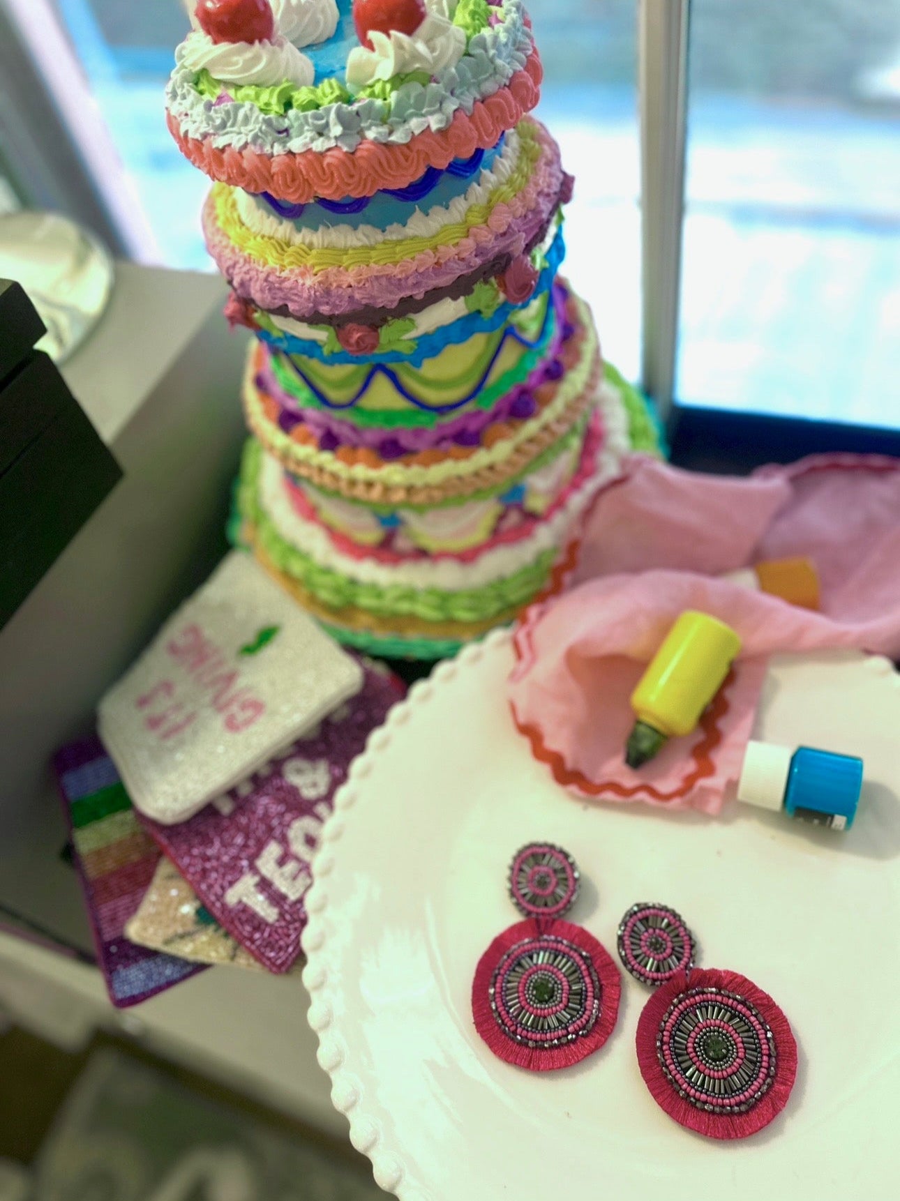 Hot pink Razzle Dazzle Pinwheel earrings styled on a white plate with colorful cake decor and glittery accessories in a vibrant party setting.