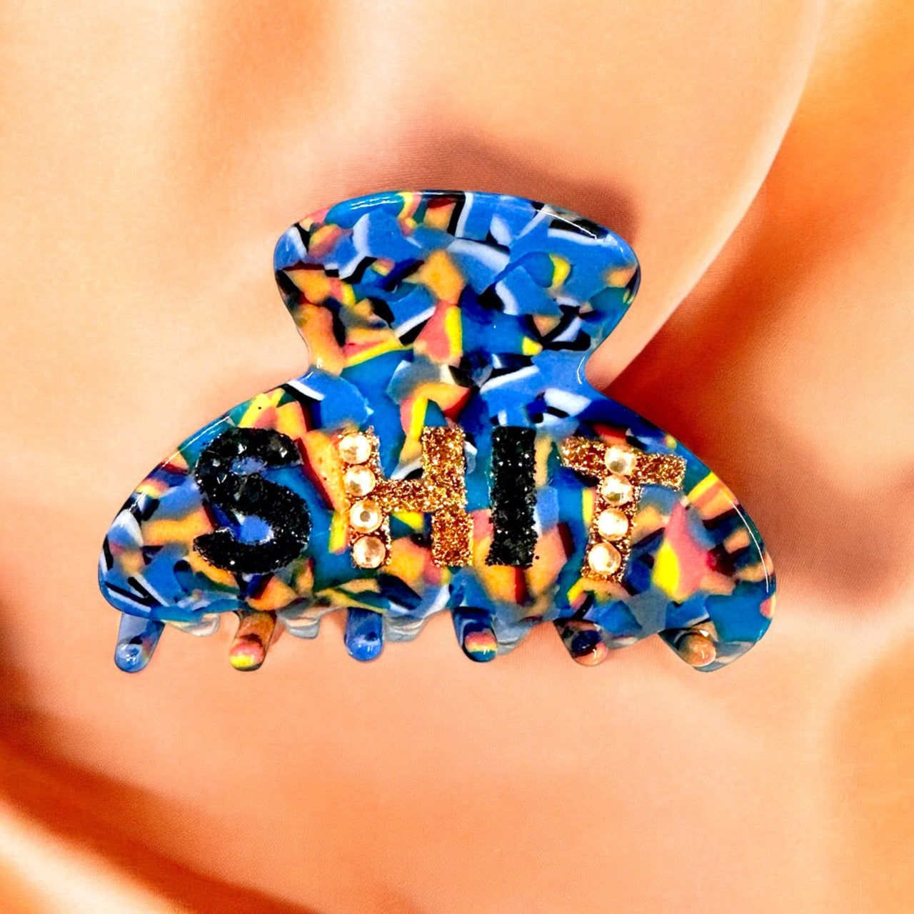 Fun "SHIT" hair clip with glitter letters and colorful design, providing secure hold for thick hair and playful styling.