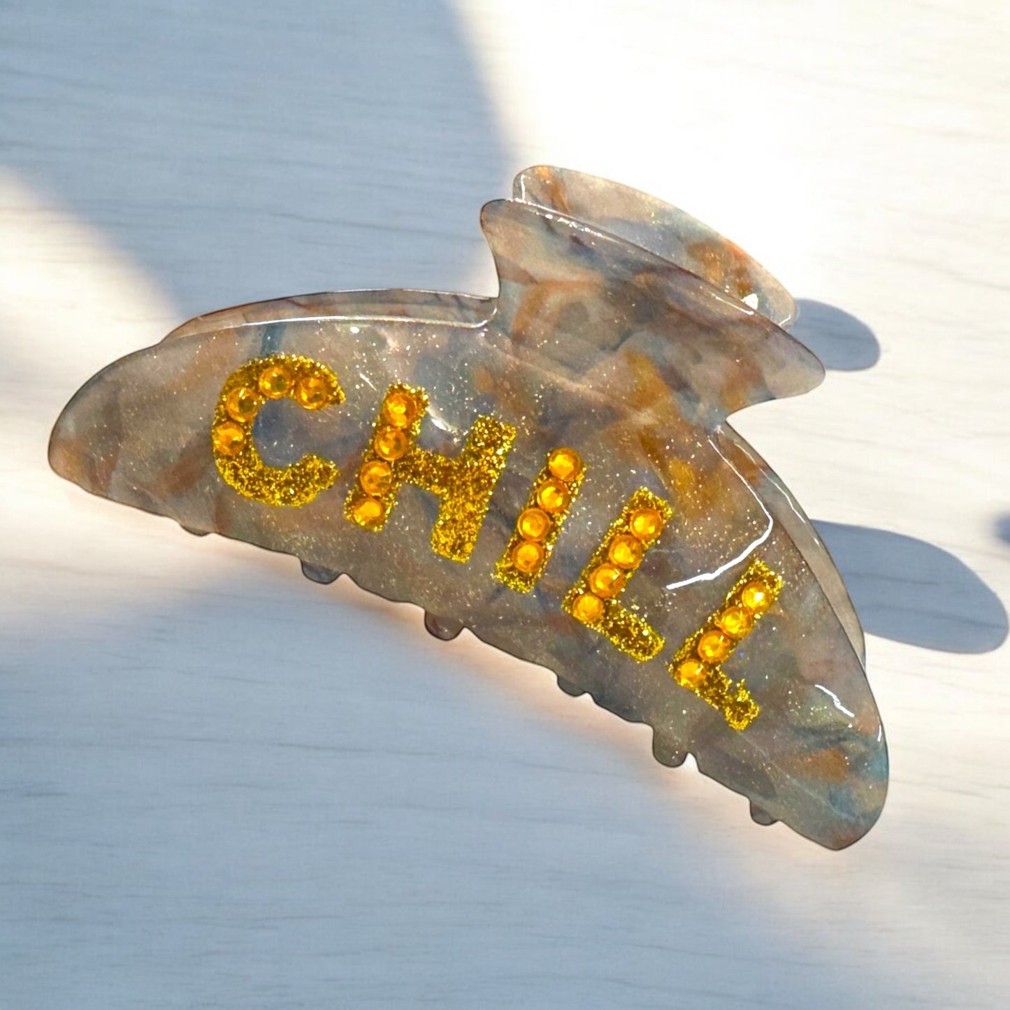 Trendy "Chill" hair clip with bold yellow glitter letters and a smoky marble base for secure hold.