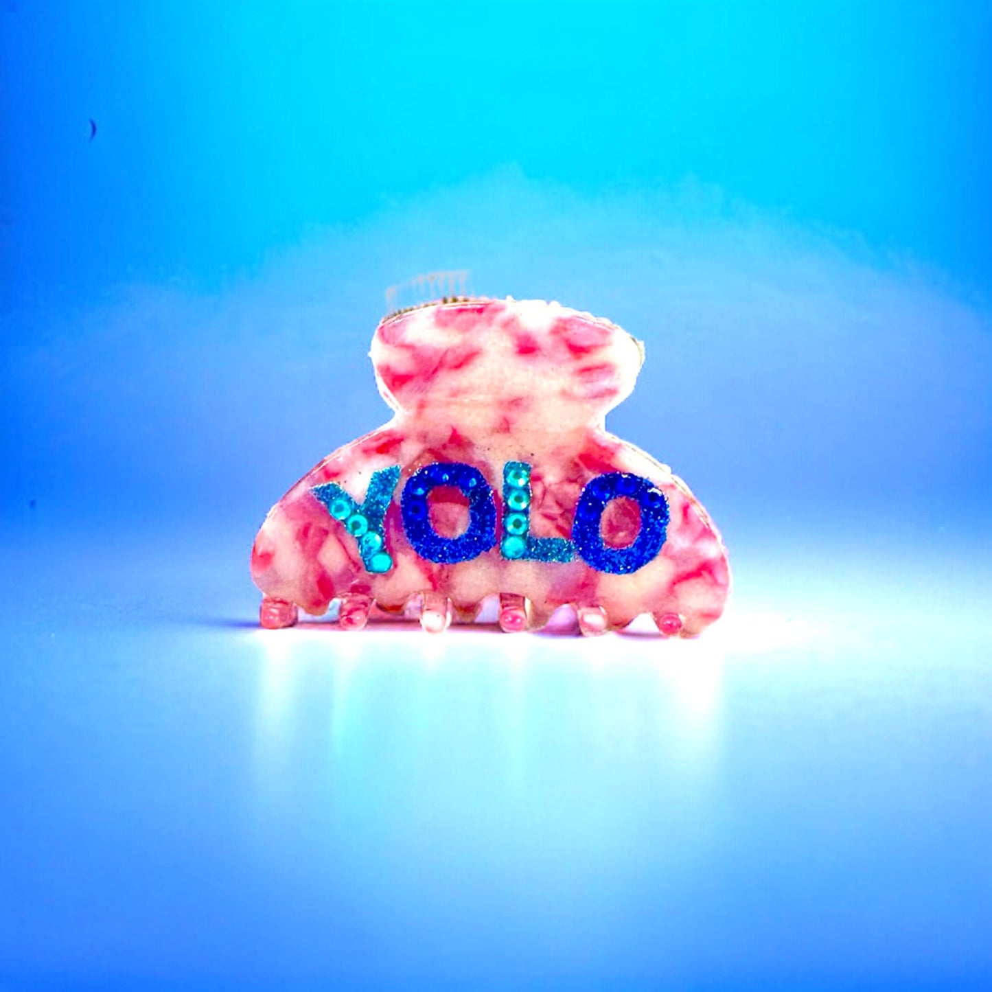 Pink hair claw clip with blue glitter YOLO design on a blue background.
