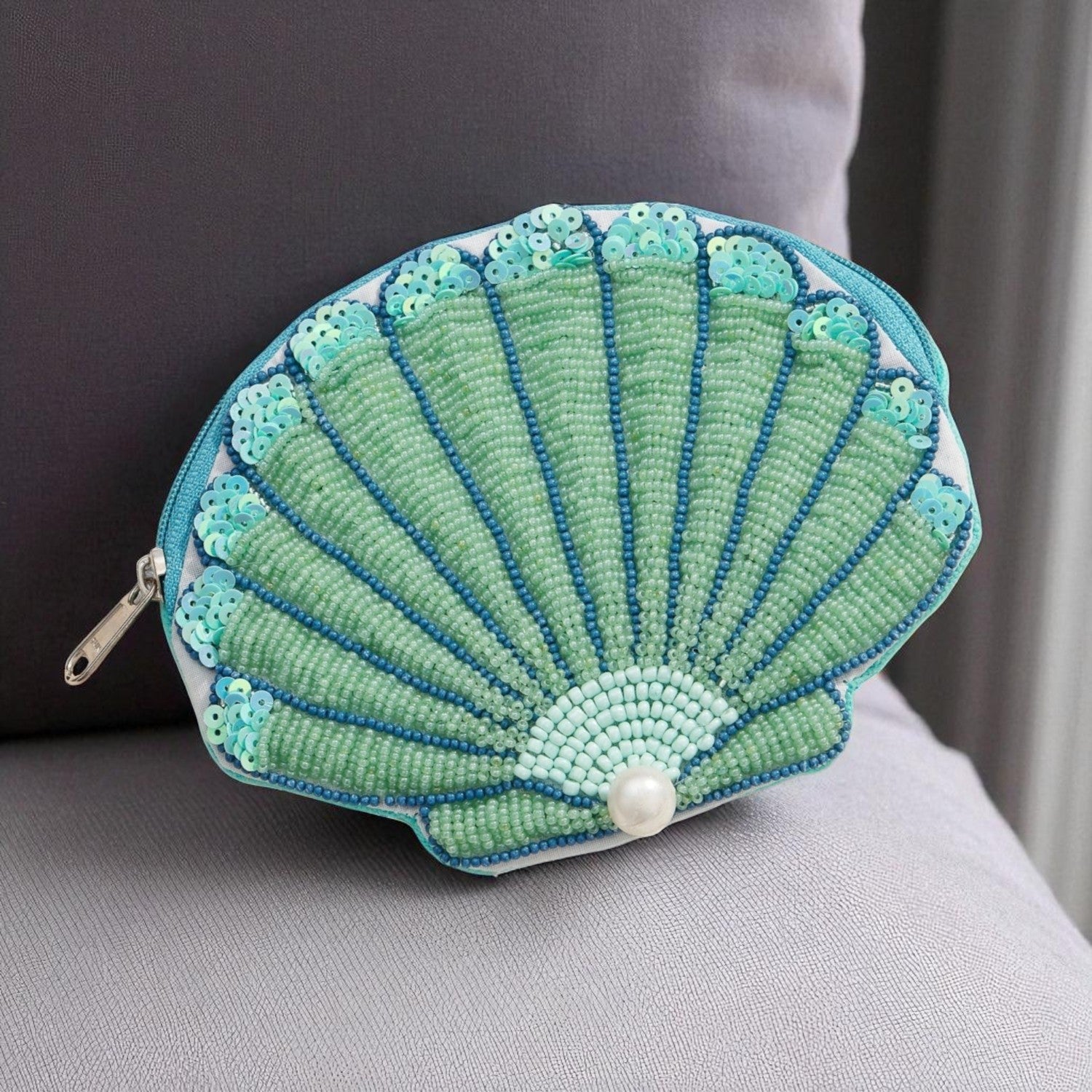 Close-up of a green beaded seashell-shaped pouch with pearl detail on a couch