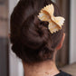 Woman wearing a farfalle pasta-shaped hair clip in a bun, showcasing a novelty foodie hair accessory.