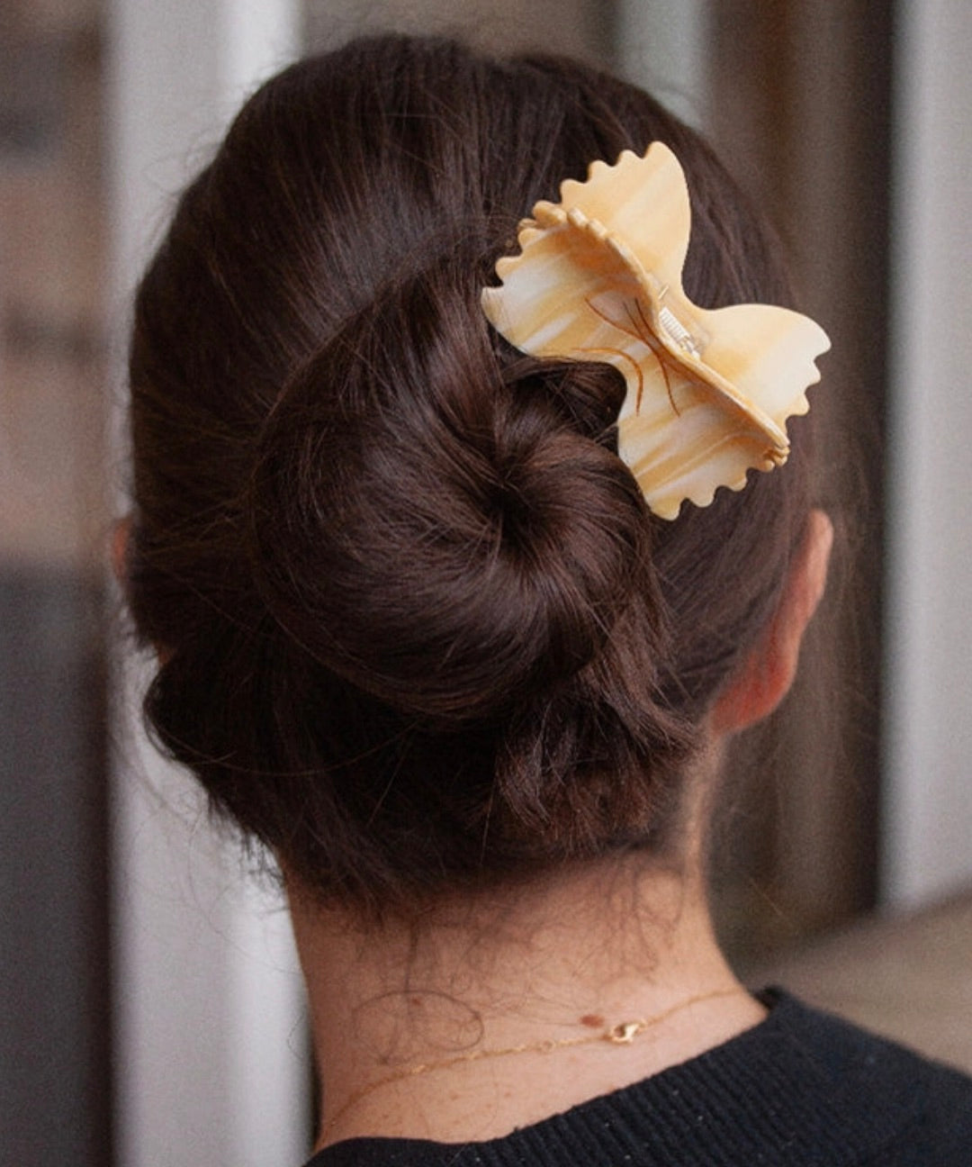 Woman wearing a farfalle pasta-shaped hair clip in a bun, showcasing a novelty foodie hair accessory.