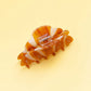 Flat lay of amber and ivory striped croissant claw clip with rhinestones on a yellow background.