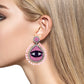 Unique pink earrings featuring evil eye, fringes, and rhinestones.
