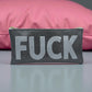 Small black glitter pouch with bold silver “FUCK” lettering, styled in front of a pink pillow.