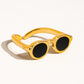 Flat lay of a bold gold ring modeled after sunglasses, placed on a white surface with visible shadowing around the edges.