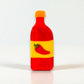 Side view of a vibrant red and yellow hot sauce bottle-shaped claw clip with pepper detail.