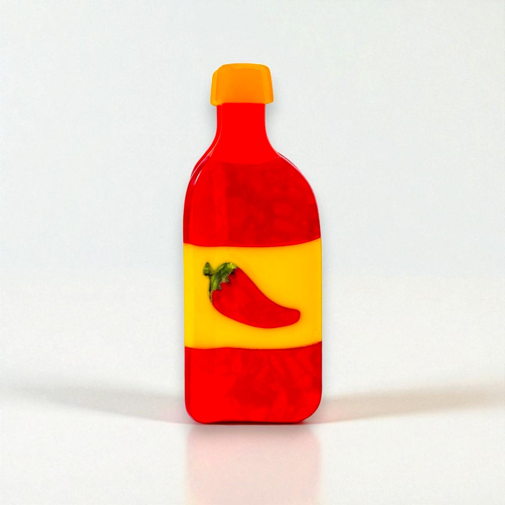Side view of a vibrant red and yellow hot sauce bottle-shaped claw clip with pepper detail.