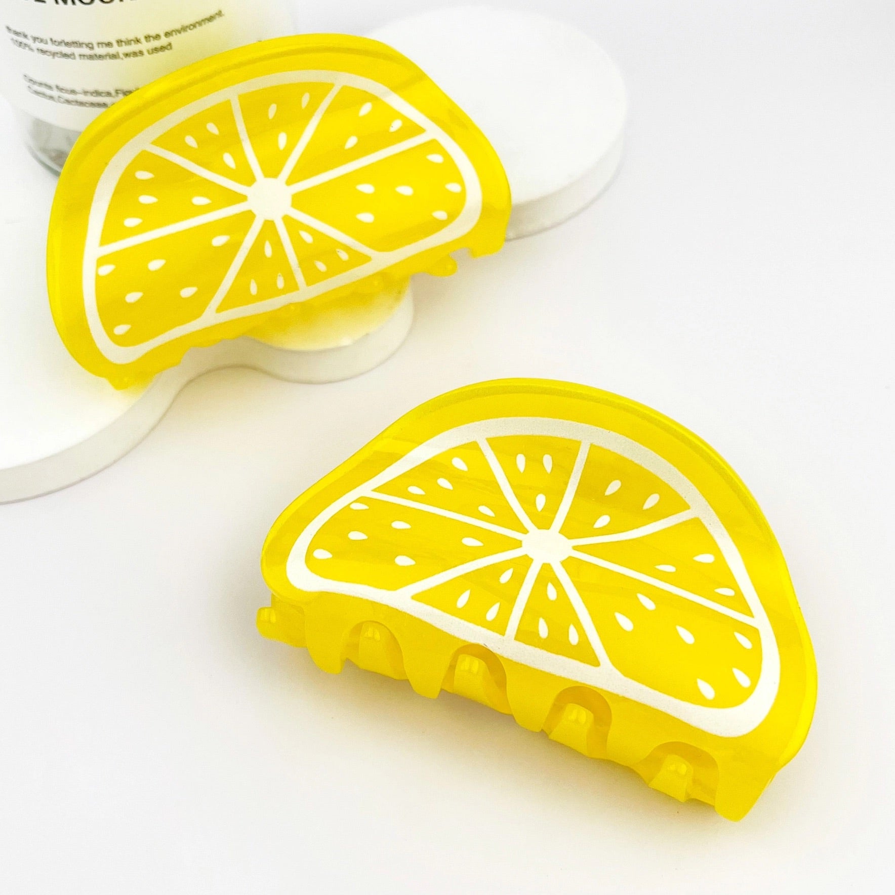 Two lemon slice hair clips in a diagonal flatlay surrounded by soft white and yellow decor.