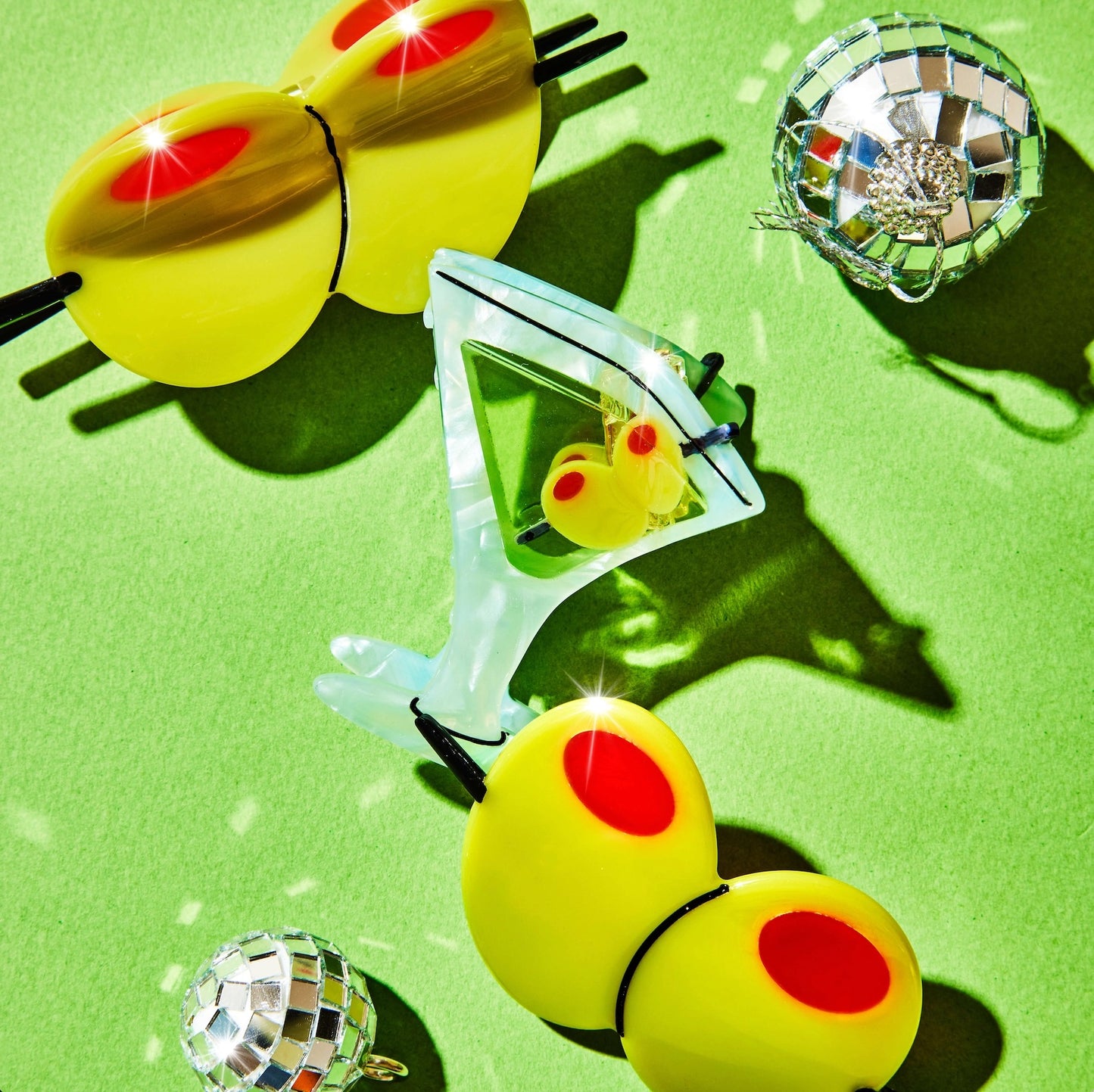 Martini hair clip styled with oversized olive props and disco balls on a green backdrop.