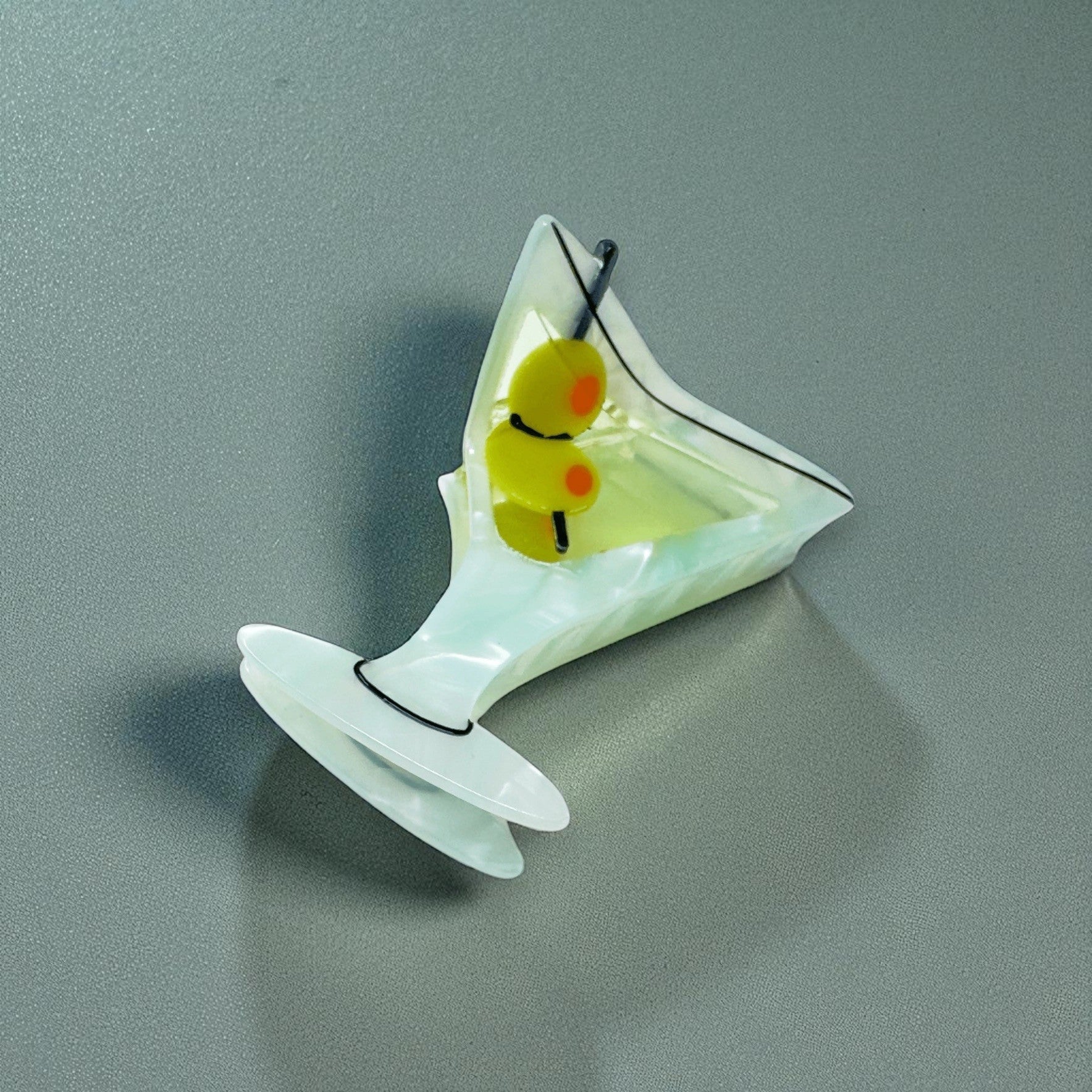 Martini glass-shaped hair clip with olive garnish, shown from the front on a grey background.