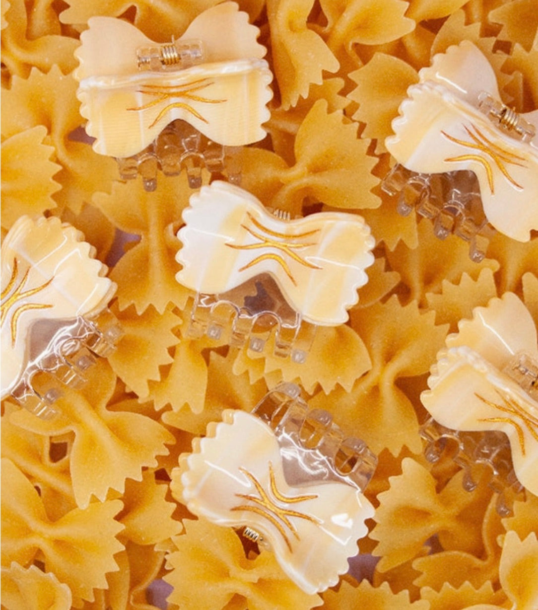 Multiple cream-colored bowtie pasta hair clips displayed on real bowtie pasta background.