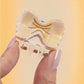 Close-up of a hand holding a mini bowtie pasta-shaped hair clip with shiny details.