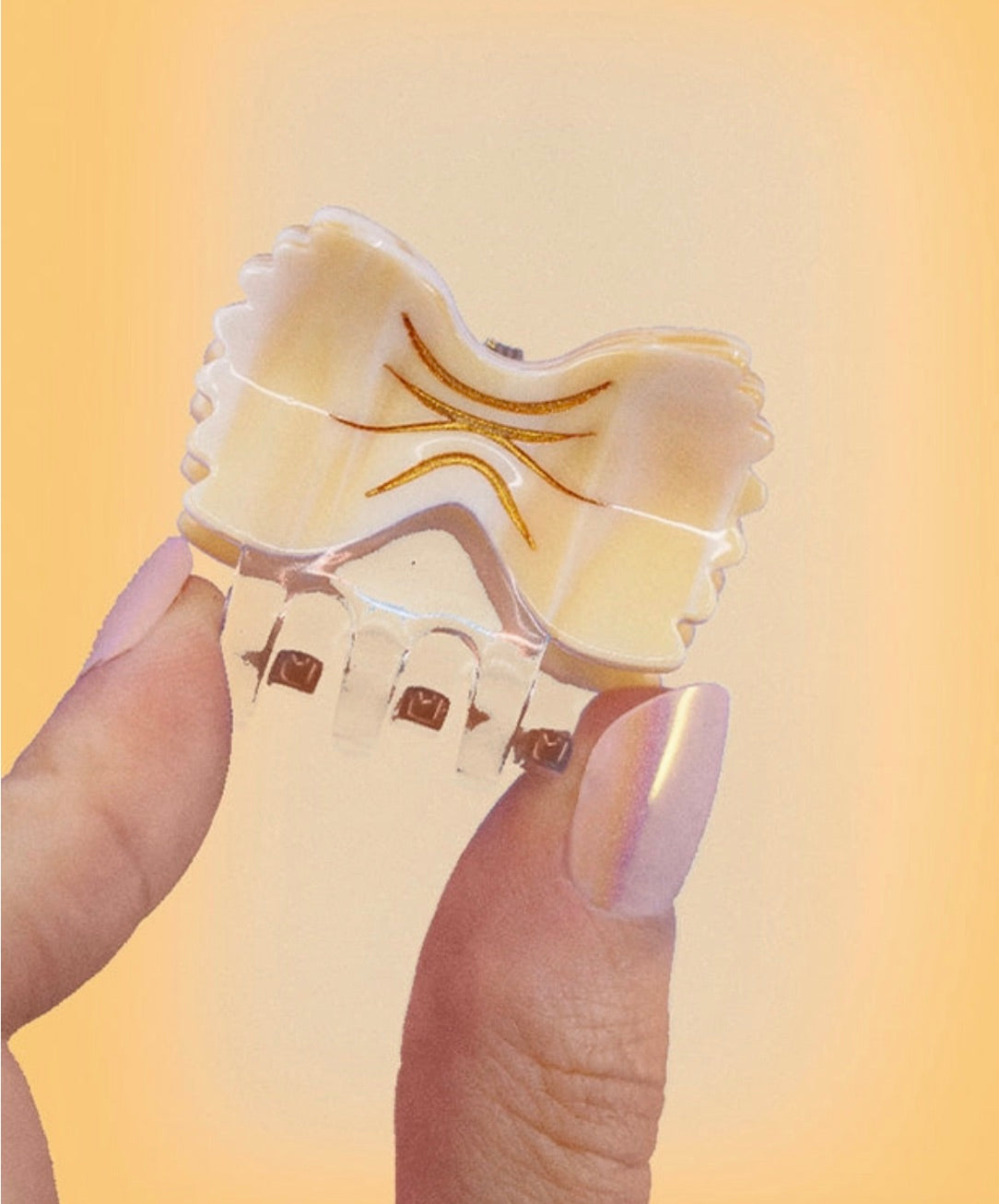 Close-up of a hand holding a mini bowtie pasta-shaped hair clip with shiny details.