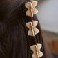 Three bowtie-shaped hair clips styled vertically in brunette hair.