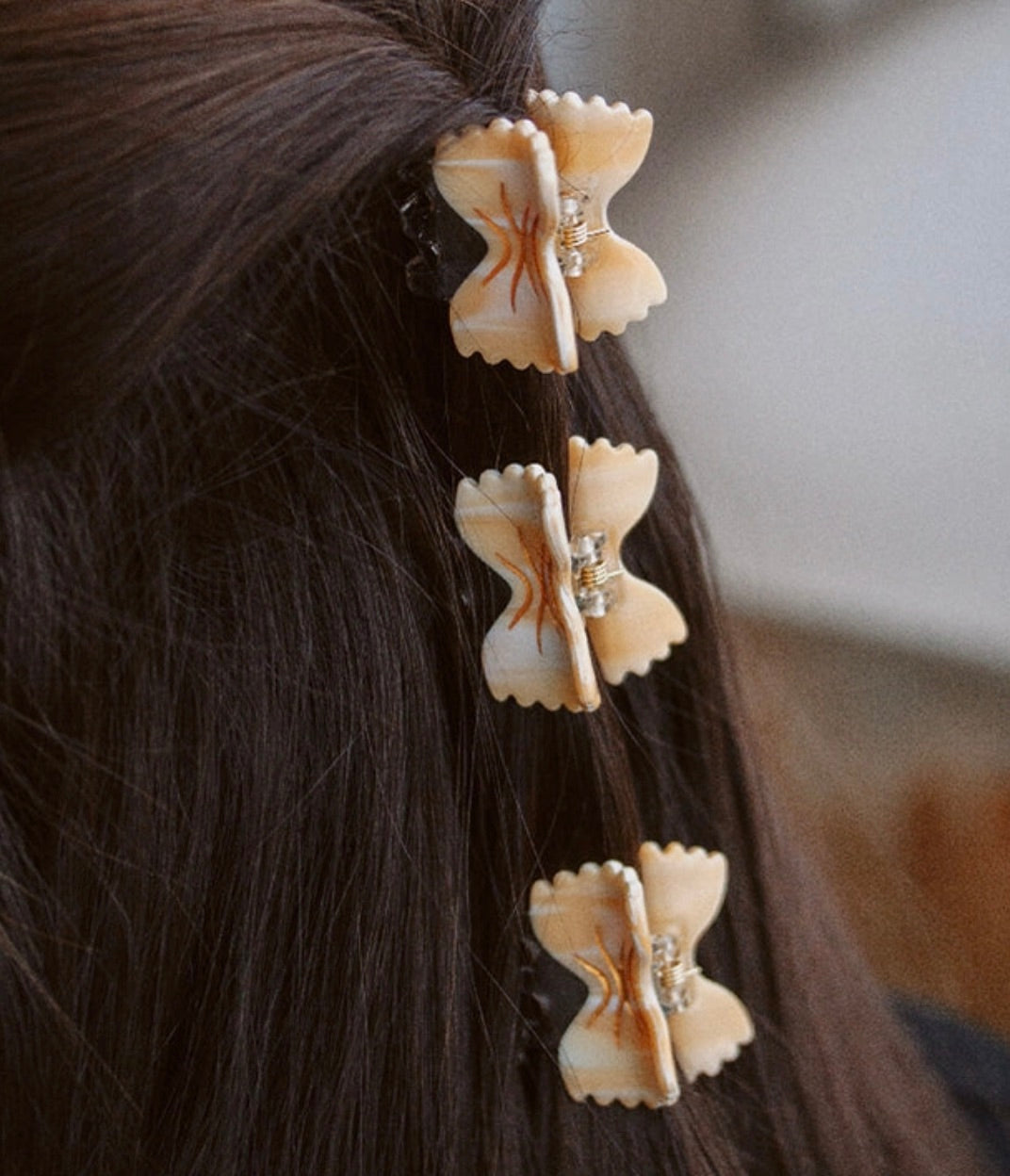Three bowtie-shaped hair clips styled vertically in brunette hair.