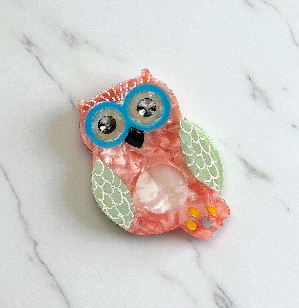 Top view of a quirky owl clip on a marble surface, highlighting green wings and crystal belly detail.