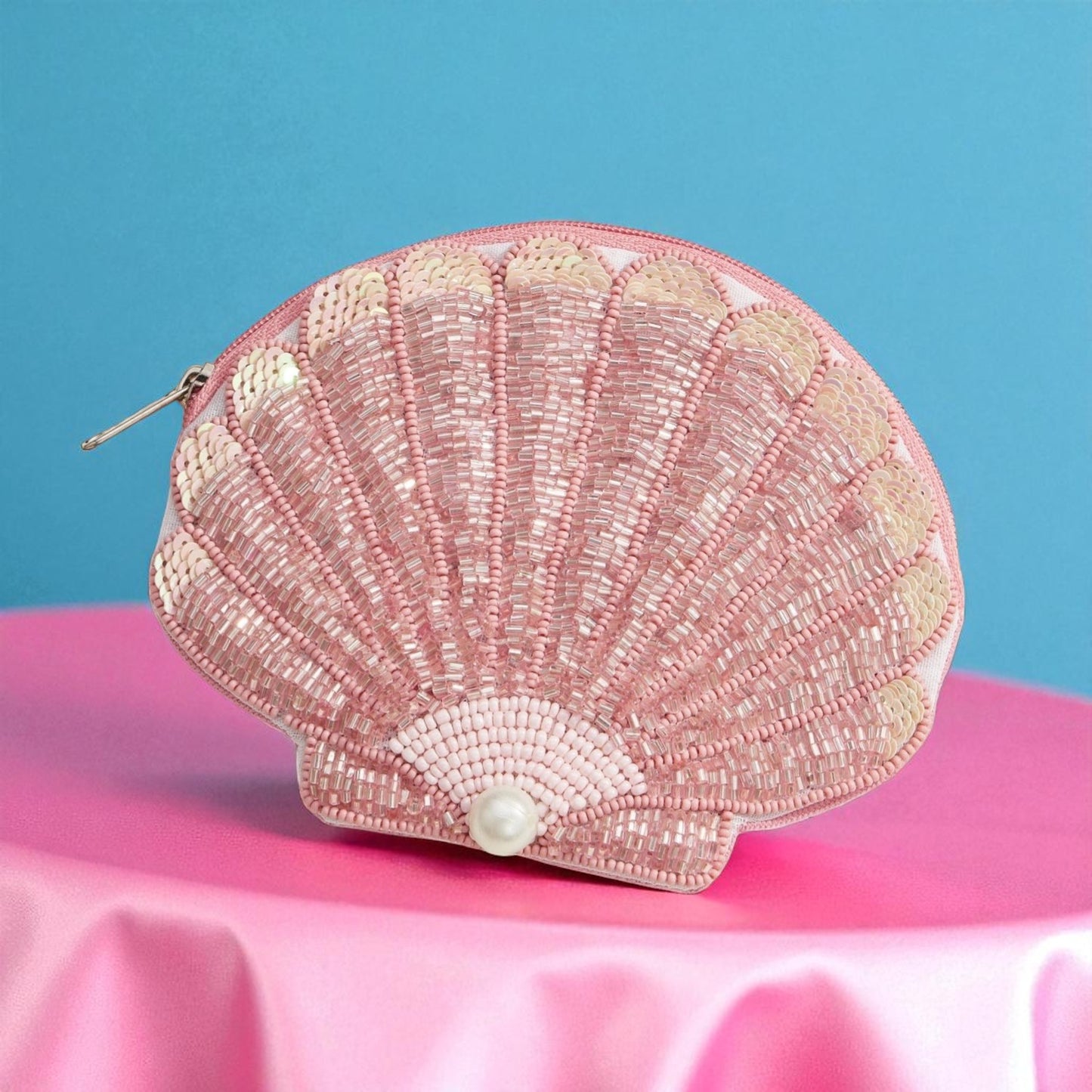 Pink beaded seashell clutch with pearl detail displayed on pink satin with blue backdrop