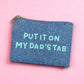 Sparkly blue beaded pouch with light teal text reading “Put It On My Dad’s Tab,” styled on a pink background.