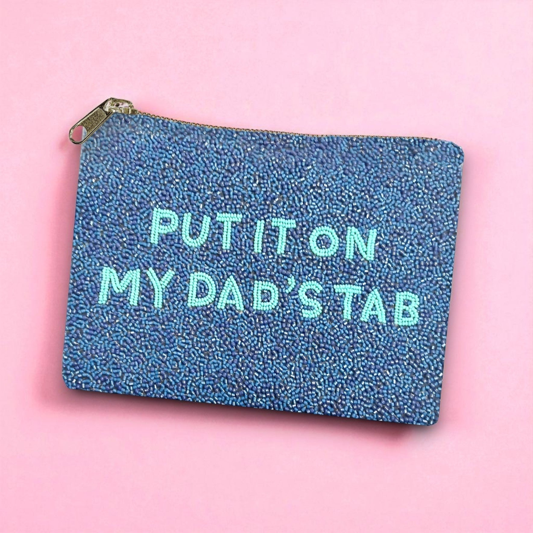 Sparkly blue beaded pouch with light teal text reading “Put It On My Dad’s Tab,” styled on a pink background.