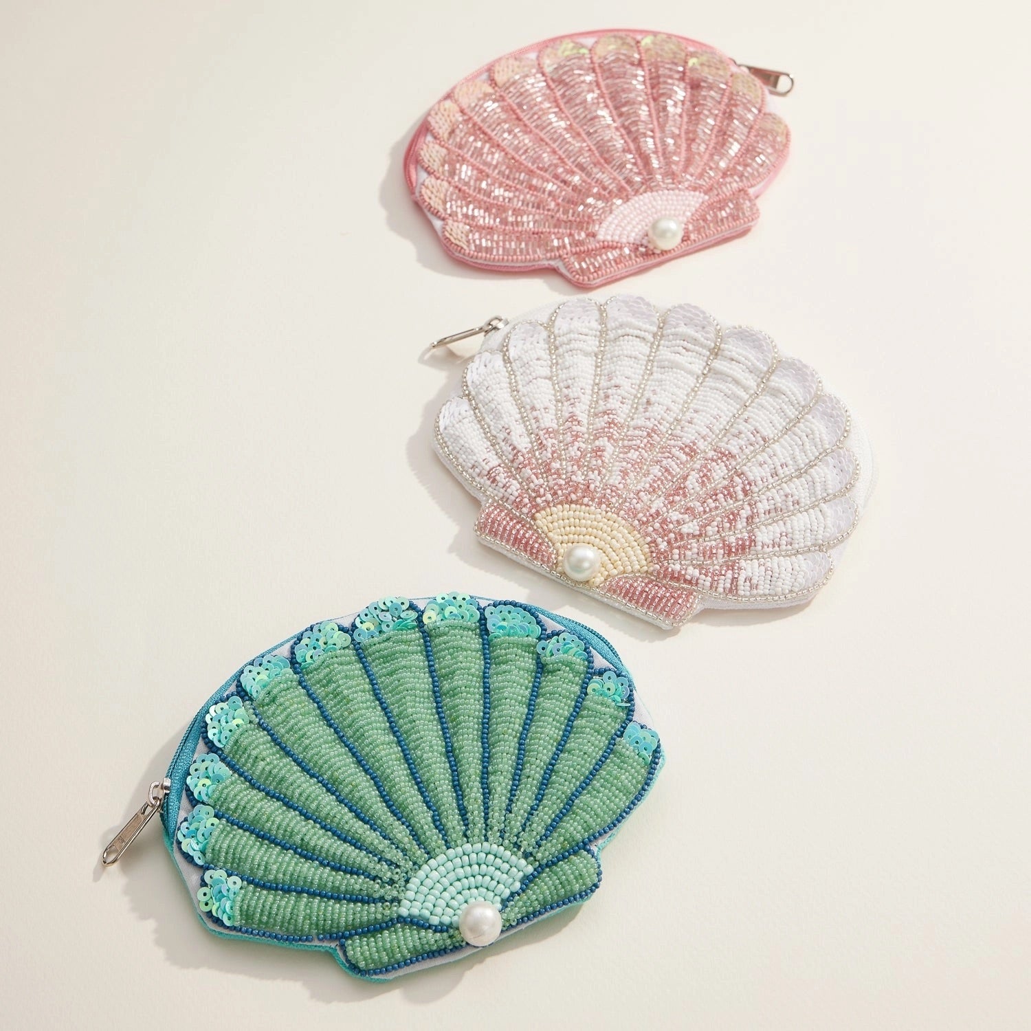 Flat lay of three shell pouches in pink, white, and green with beaded details and pearl embellishments