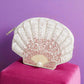 Beaded shell pouch in white and pink ombré displayed upright on a magenta block against a purple background.