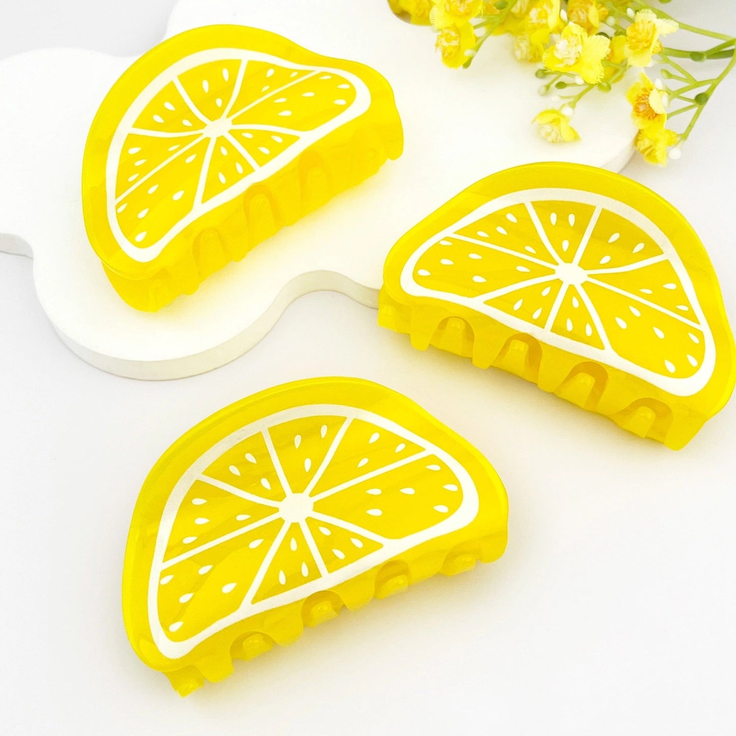 Flat lay of three yellow lemon slice claw clips styled on white background with floral accents.