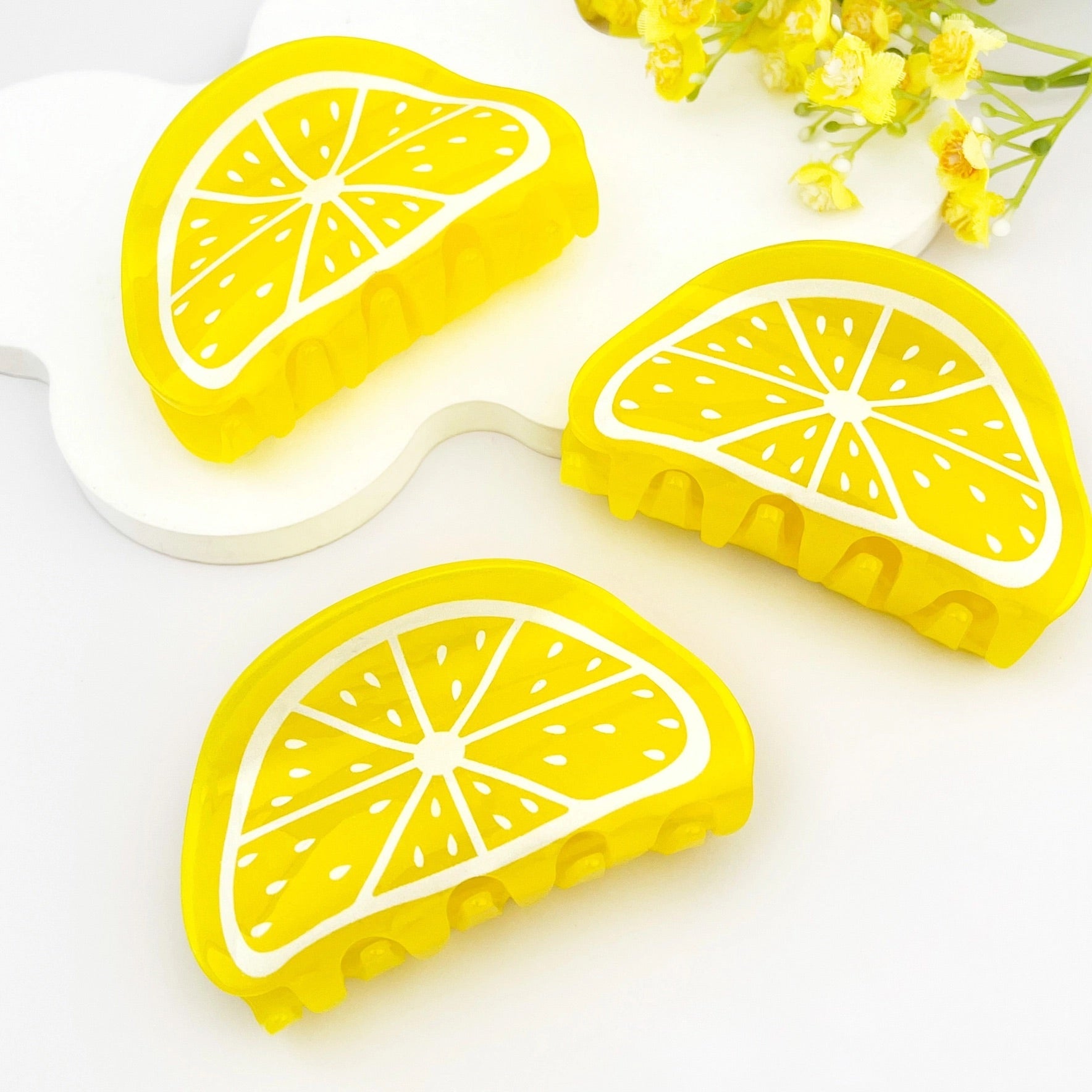 Flat lay of three yellow lemon slice claw clips styled on white background with floral accents.