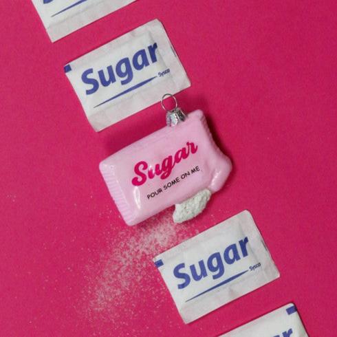 Pink glass ornament shaped like a sugar packet with playful "Pour Some on Me" message, perfect for Christmas trees.