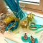 Aqua teardrop fringe earrings with beaded detail, styled with turquoise ribbon, blue straws, scissors, and star-shaped candles for a creative summer vibe.