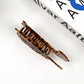 Top-down view of a classic tortoise shell hair claw clip placed on a white background near a book.