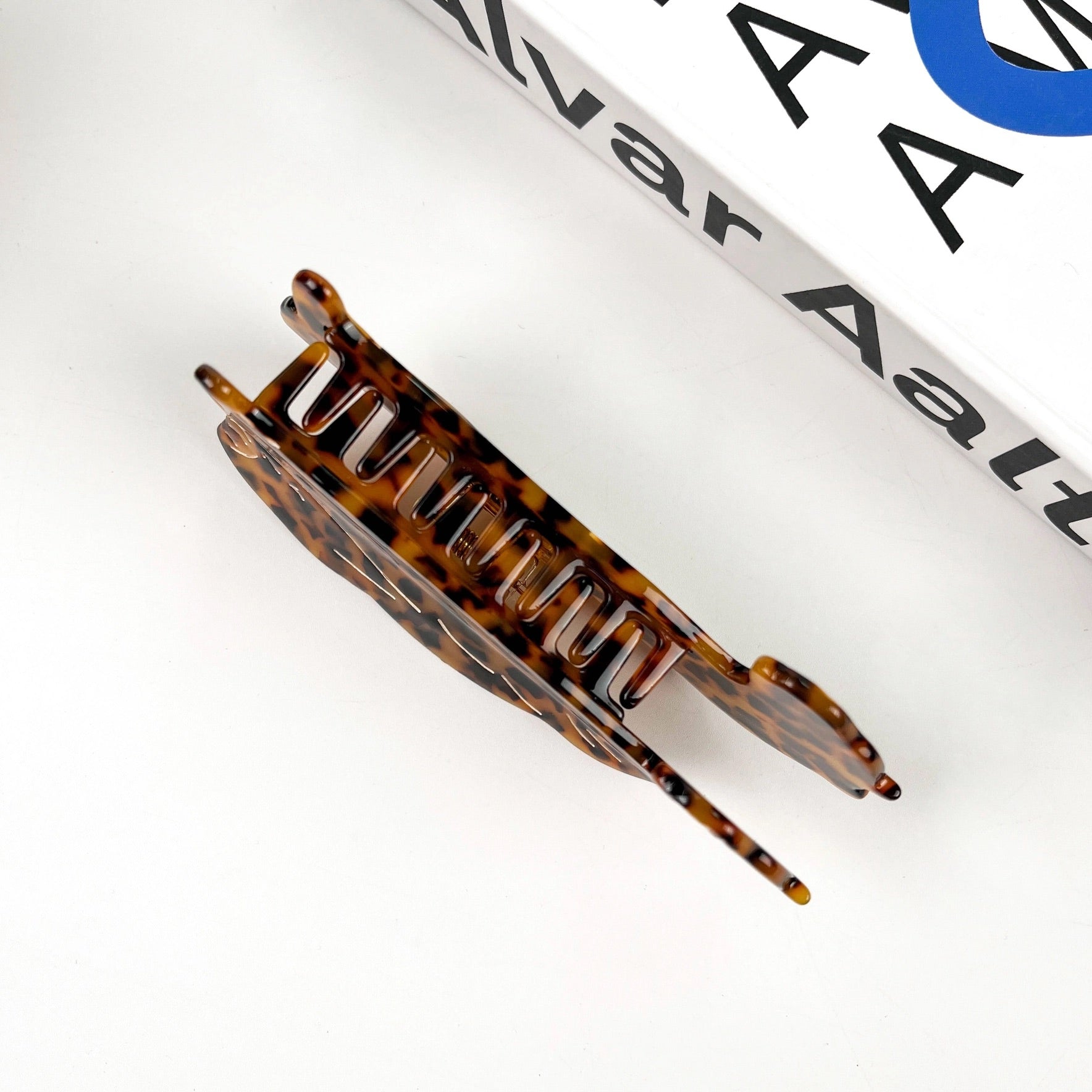 Top-down view of a classic tortoise shell hair claw clip placed on a white background near a book.