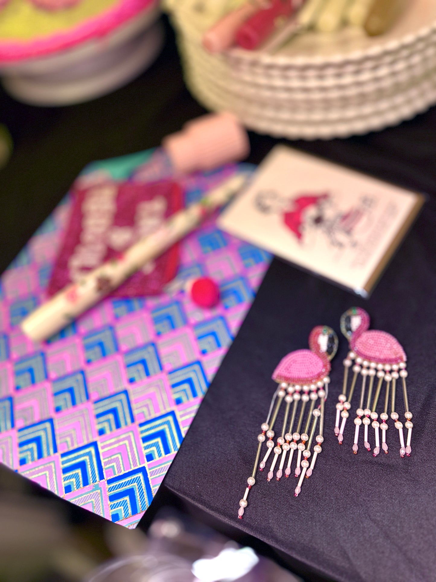 Playful pink flamingo statement earrings styled beside plates, a lipstick, and party supplies for a cheeky, feminine tabletop party flatlay.